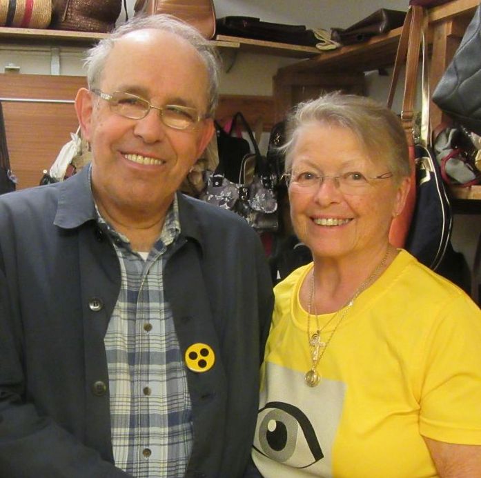 älterer Mann und ältere Frau mit gelbem Hilfsgemeinschaft-T-Shirt lächeln in die Kamera