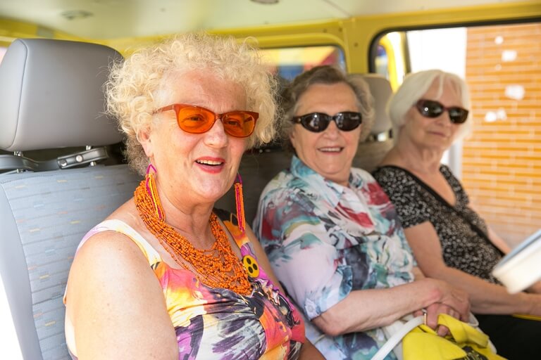 Drei Damen mit Sonnenbrillen sitzen lächelnd im Kleinbus.
