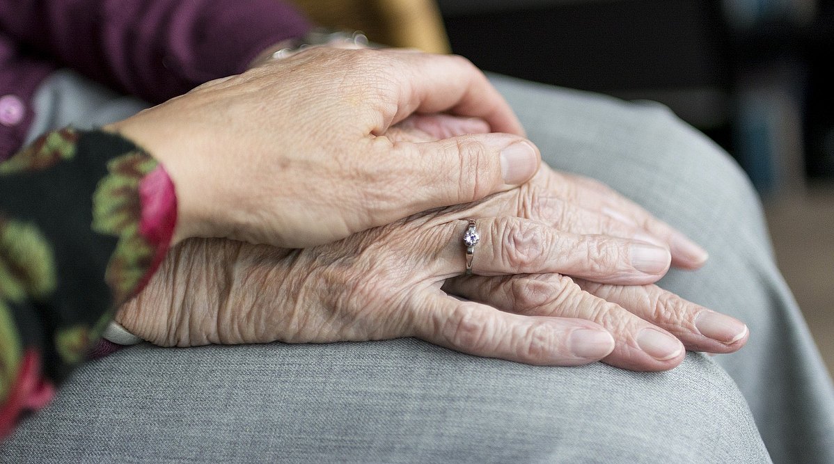 Symbolbild die Hand einer jungen Frau sanft auf den Händen einer älteren Dame liegend.