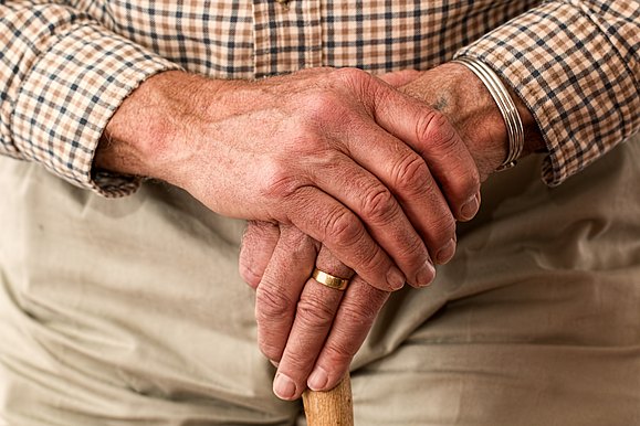 Symbolbild Nahaufnahme Hände von Senior gefaltet auf einem Gehstock ruhend.